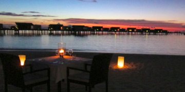 a table and chairs on a beach with a sunset in the background