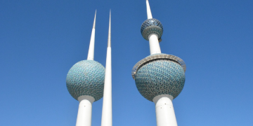 a group of tall towers with blue and white balls with Kuwait Towers in the background