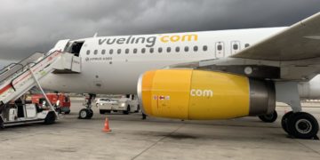 a white airplane with yellow engine and a white car on the tarmac