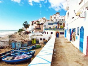 a white building with blue doors and boats on the shore