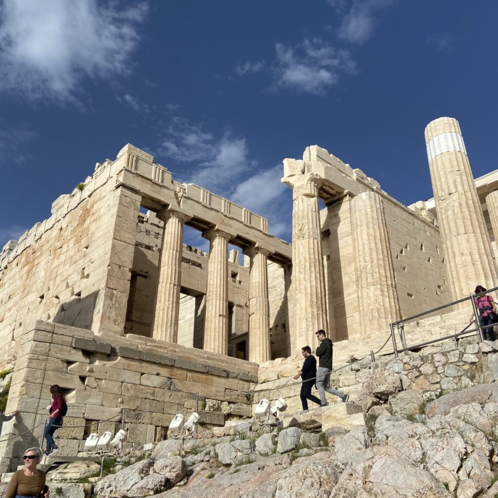 a stone building with columns with Acropolis of Athens in the background