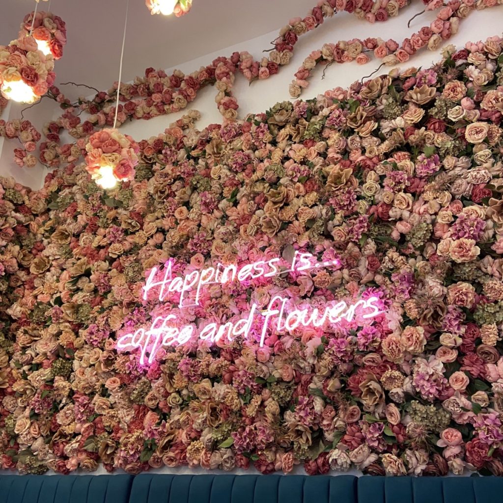 a wall of flowers with a neon sign