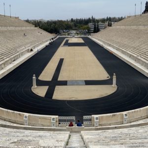 a stadium with a track and seats with Panathenaic Stadium in the background