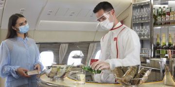 a man wearing face mask and white coat standing at a counter in an airplane