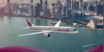 a plane flying over water with a city in the background