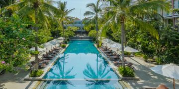 a pool with lounge chairs and umbrellas surrounded by palm trees