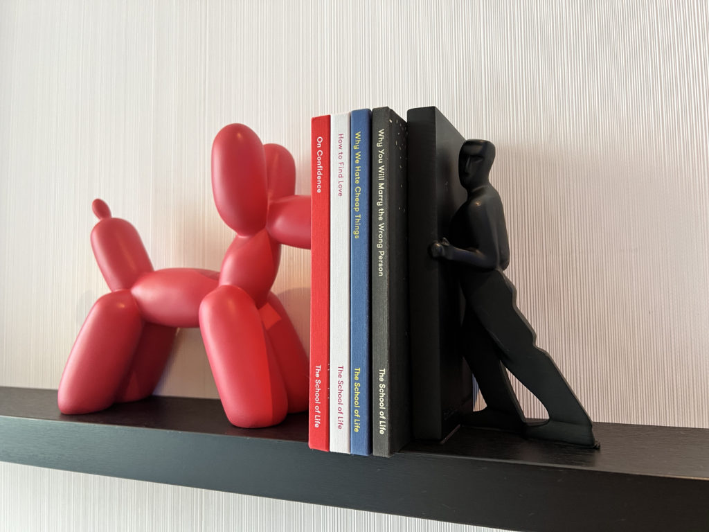 a red balloon dog figurine leaning on a black book shelf