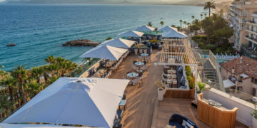 a rooftop restaurant with tables and umbrellas overlooking the ocean