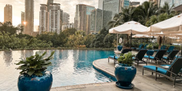 a pool with chairs and umbrellas in front of a city